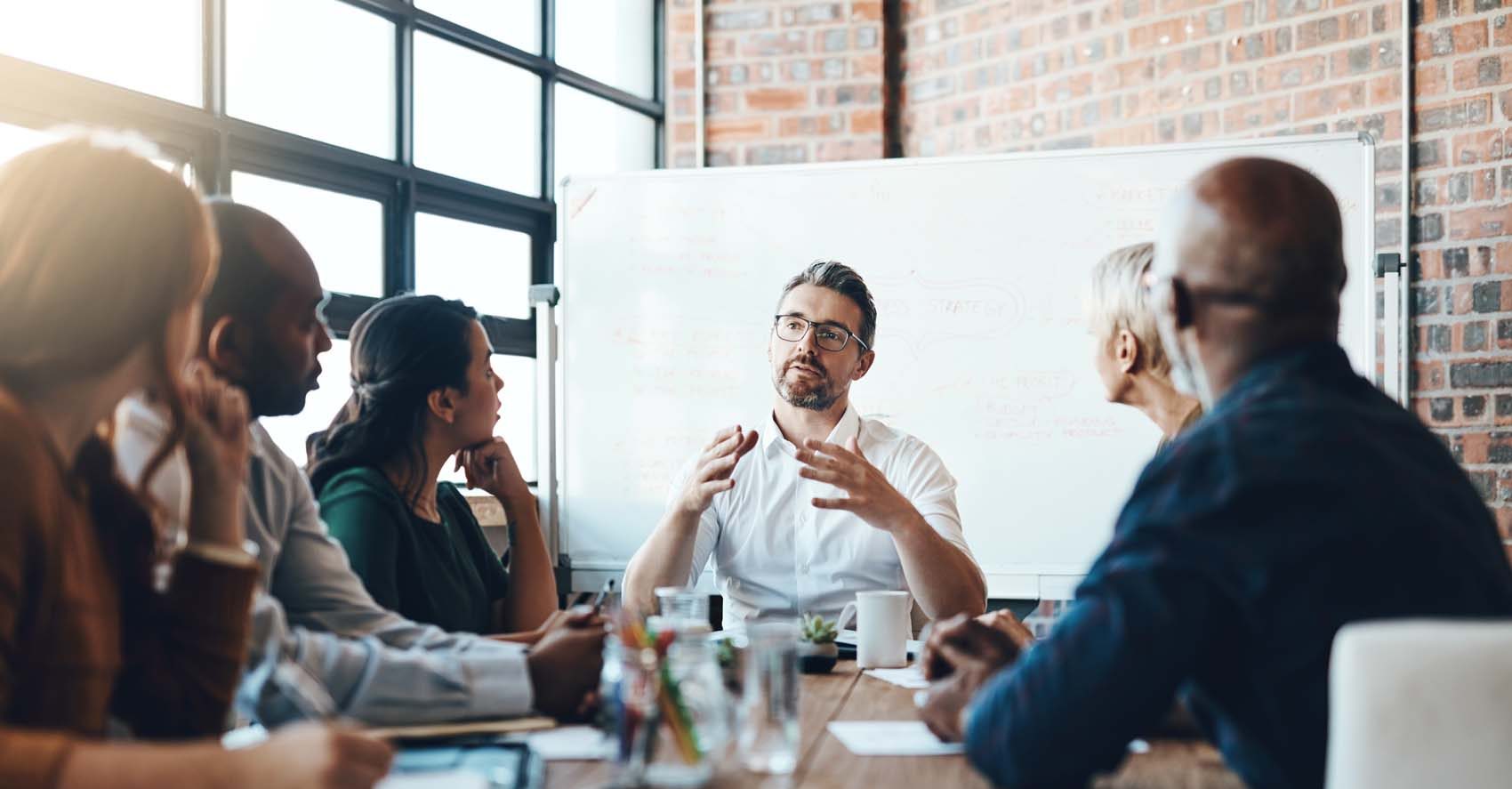 A man in a white shirt talking to a group of people at a table.