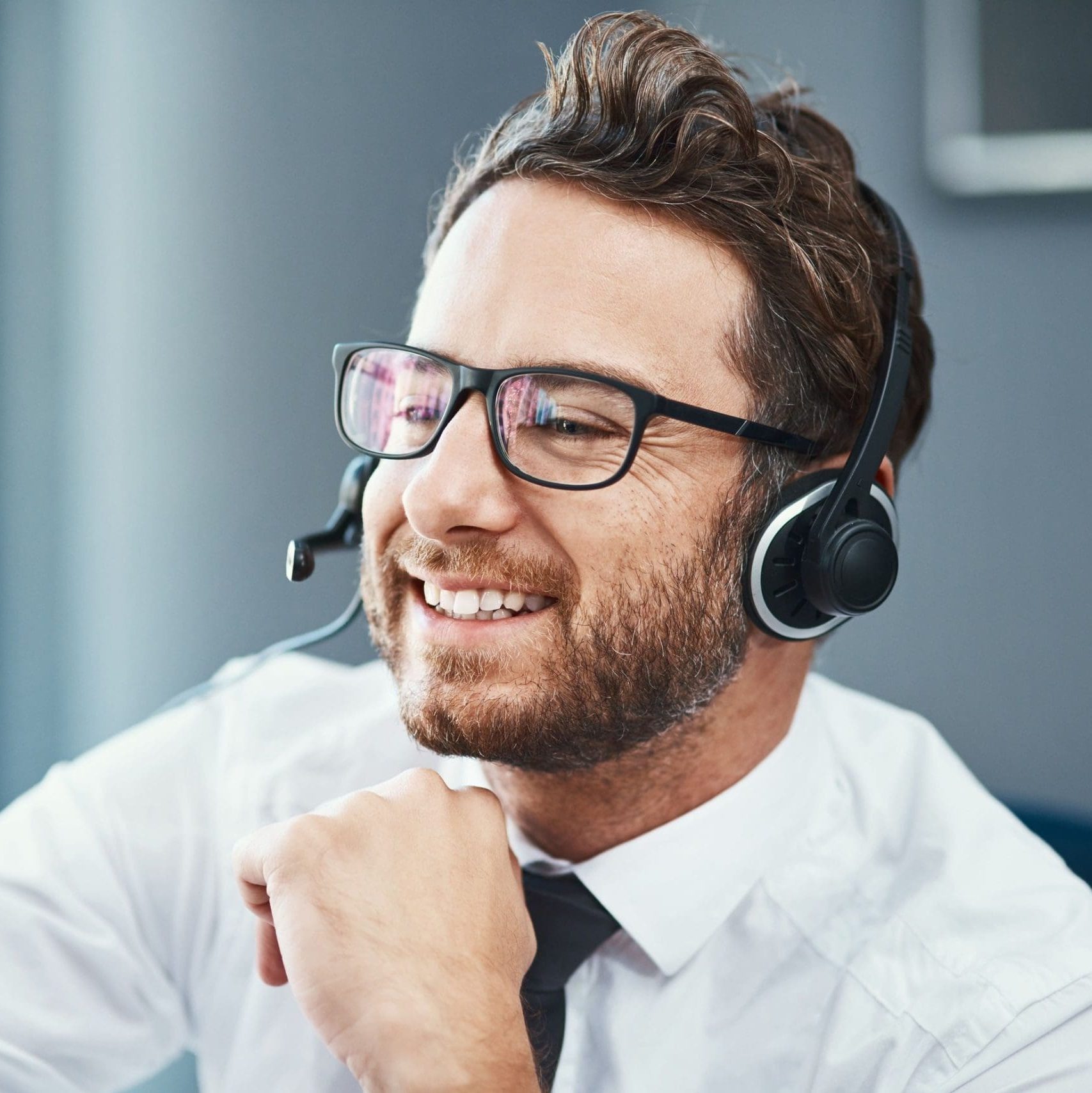 A friendly man communicating with a client while wearing a headset and a white shirt.