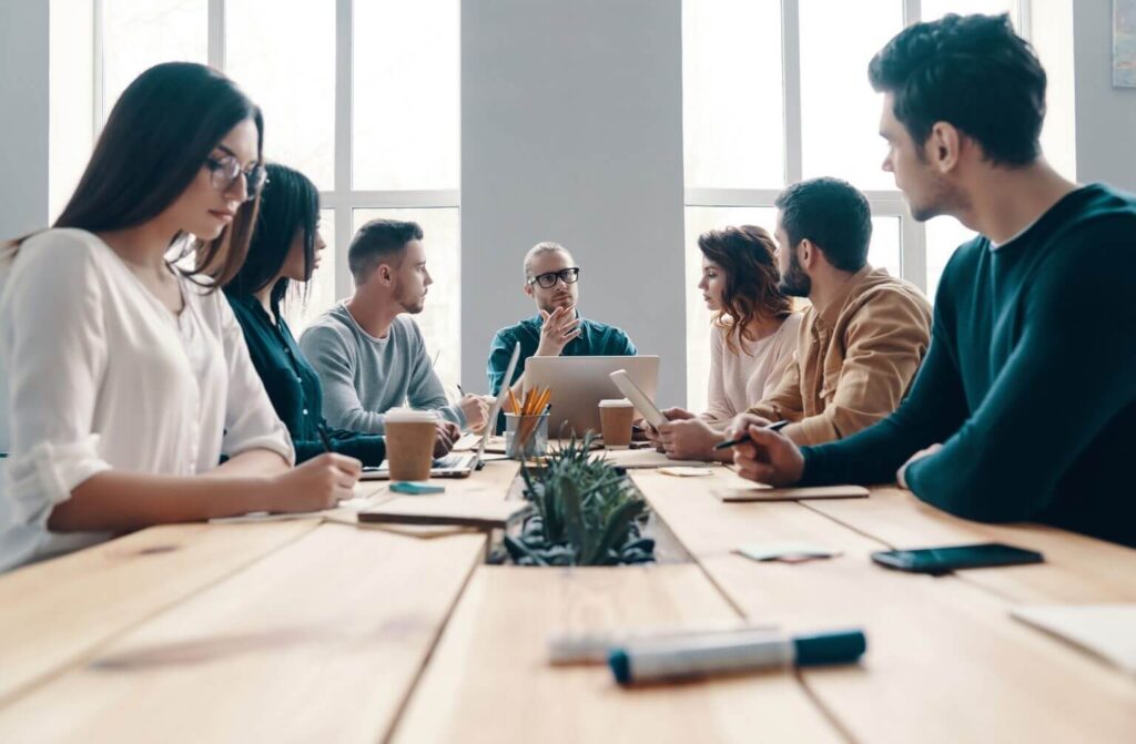 a group of seven colleagues meeting at a table in a corporate office environment 