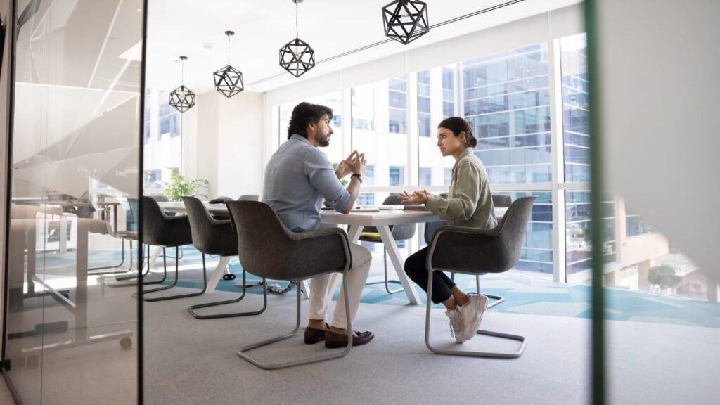 male and female colleagues sat across from each other at a desk in a corporate office